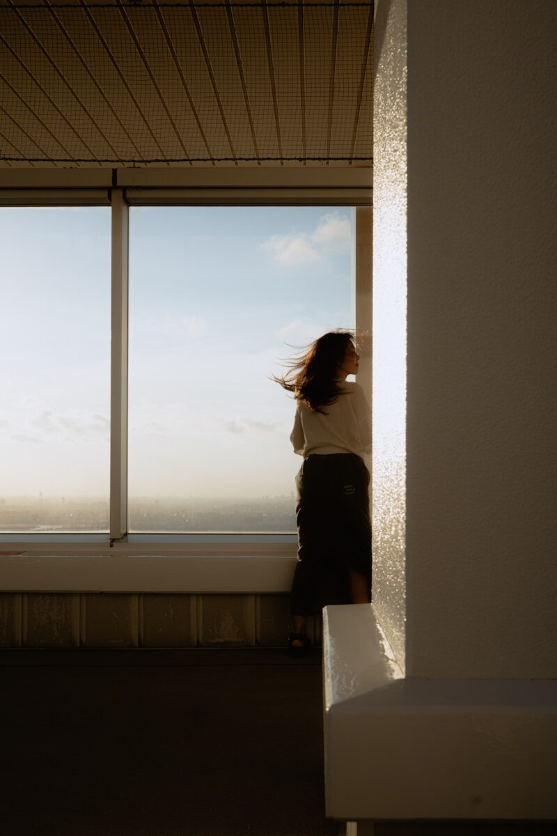 Woman looking out a large window at sunset